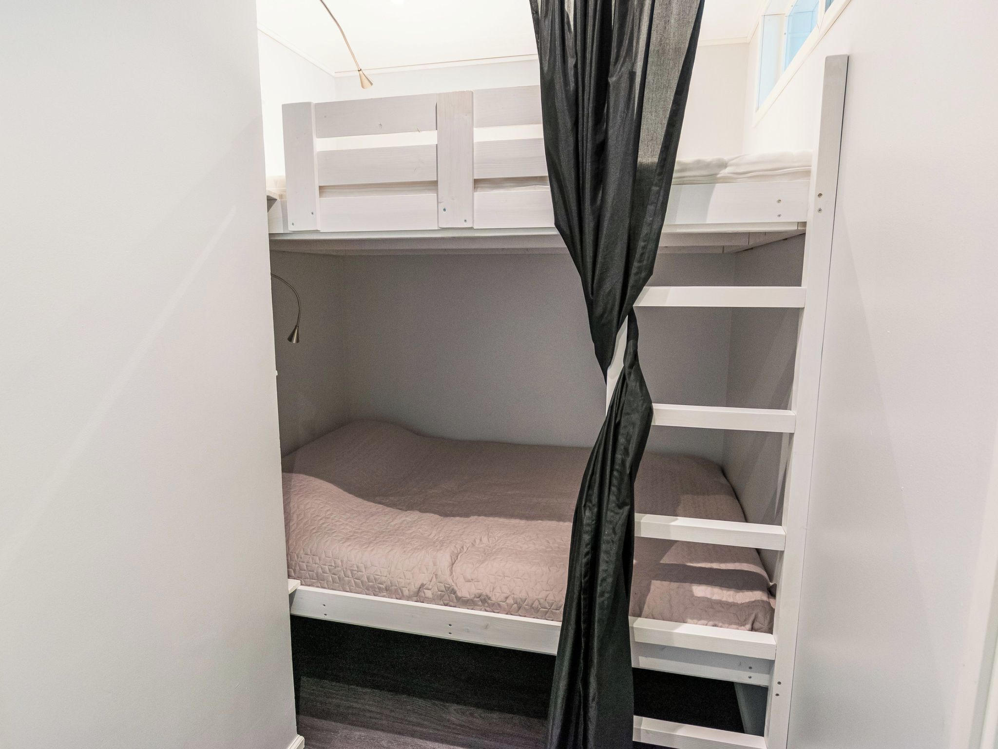Uma cama beliche com cortina, uma escrivaninha e uma cadeira.