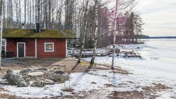 A small red cabin with a wooden deck and a dock extending into a frozen lake.