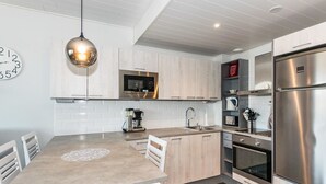 Une cuisine moderne avec des meubles en bois clair, des appareils en acier inoxydable et un îlot central doté de sièges.