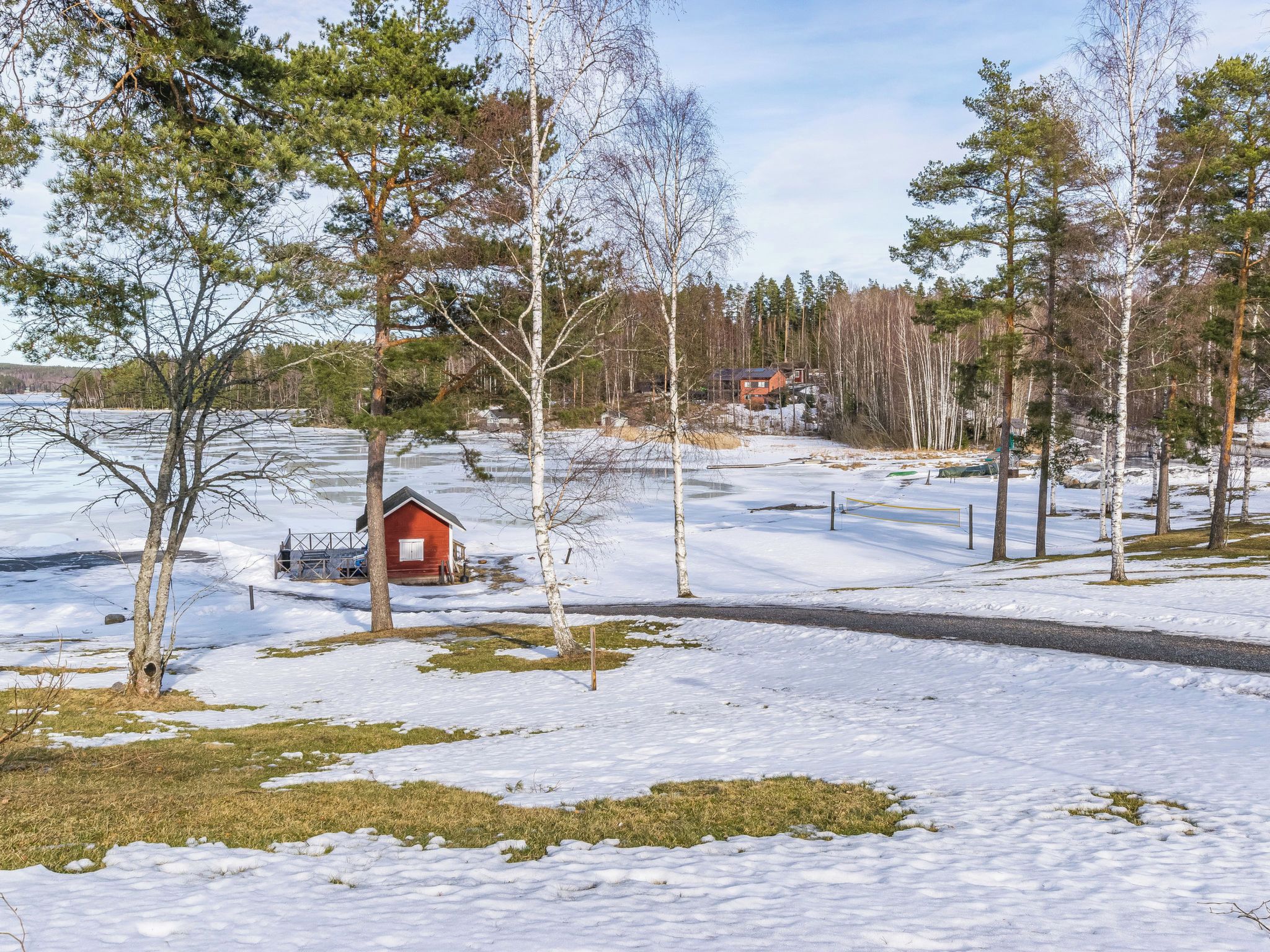 A snowy landscape with a small red cabin, trees, and a clear sky.