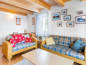 A cozy living room with two sofas, a coffee table, and a wooden ceiling.