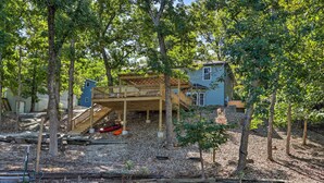 A house with a wooden deck, a small boat, and a pond. - Dock & Jet Ski Slip: Lakeside Sunrise Beach Home! (Sunrise Beach)