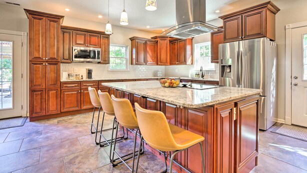 A modern kitchen with wooden cabinets, stainless steel appliances, and a central island with bar stools. - Dock & Jet Ski Slip: Lakeside Sunrise Beach Home! (Sunrise Beach)