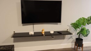 Un televisor de pantalla plana montado en la pared sobre un estante negro con tres objetos blancos.