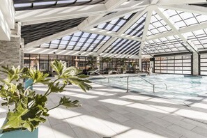 A spacious indoor swimming pool with a high ceiling and skylights, surrounded by potted plants and a seating area. - Westgate 4409 AB (Park City)