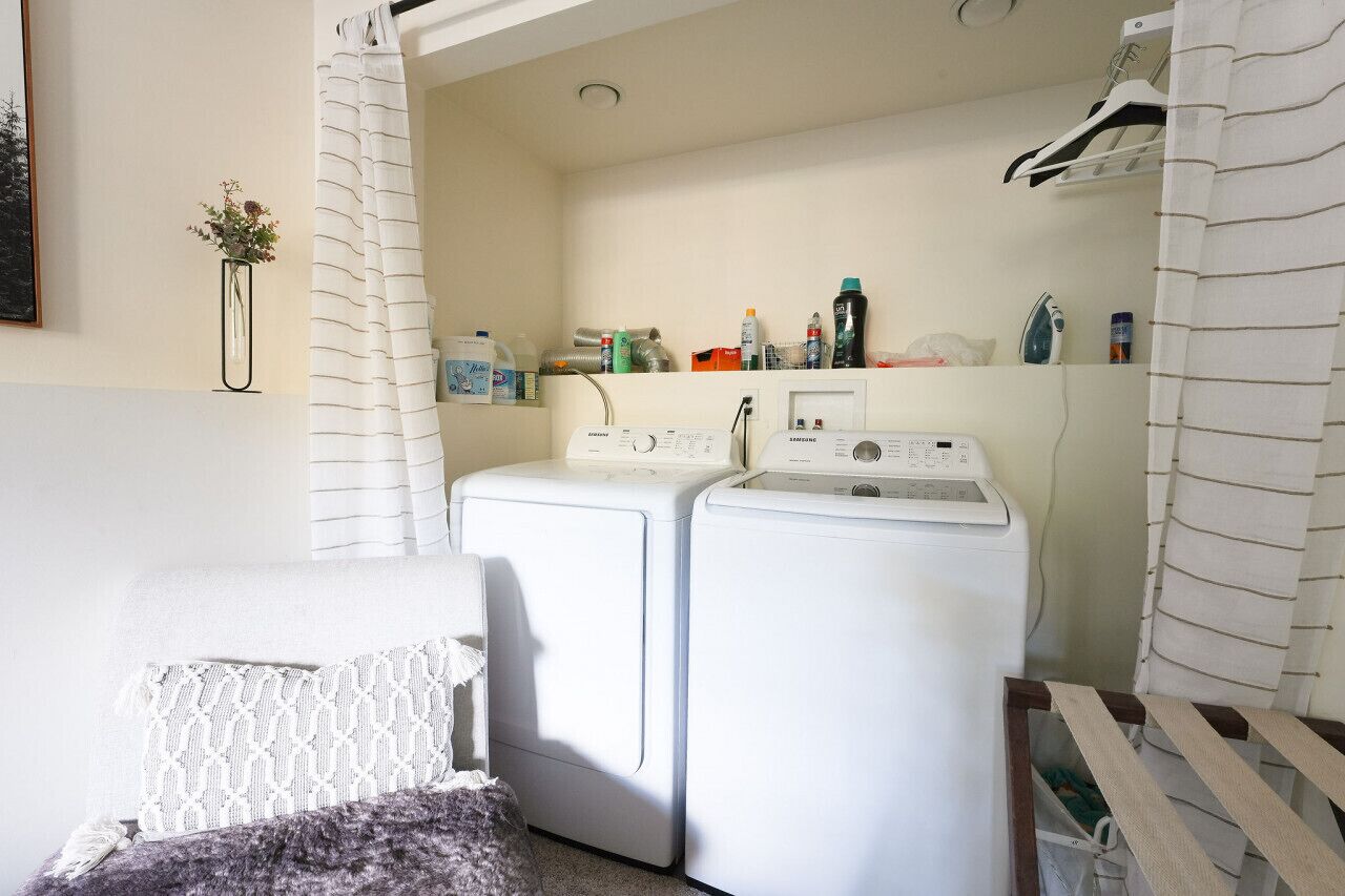 A laundry area with two white washing machines, a shelf with various cleaning products, and a hanging rack.