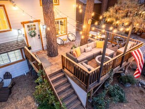A wooden deck with a sofa and chairs, surrounded by trees and string lights.