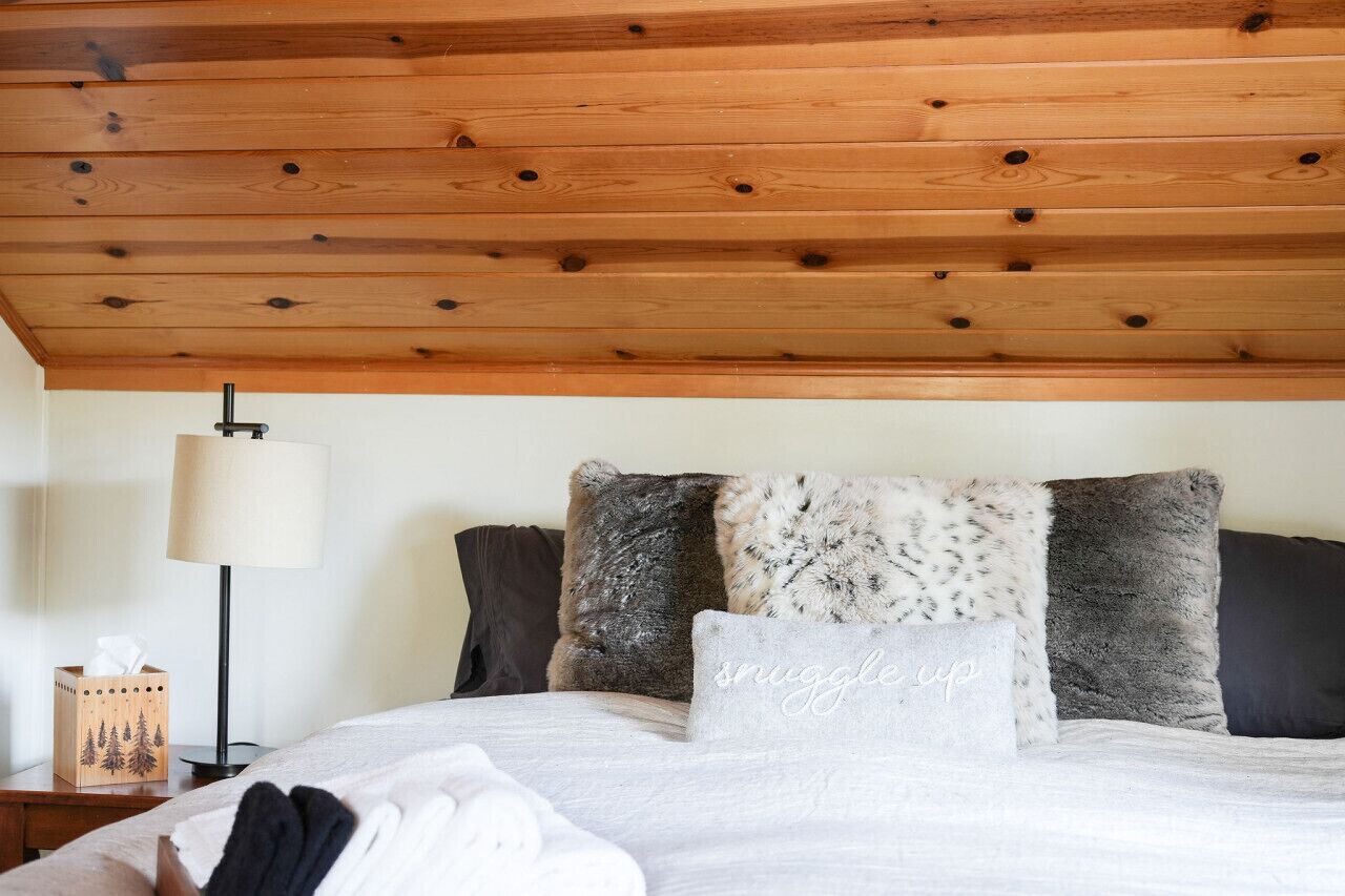 Una cama bien hecha con una variedad de almohadas, una lámpara de noche y un cabecero de madera.