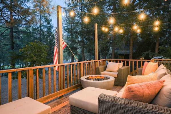 A wooden deck with outdoor seating, a fire pit, and string lights.