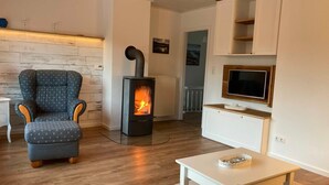 A modern living room with a wood-burning stove, a comfortable armchair, a TV mounted on the wall, and a minimalist design.