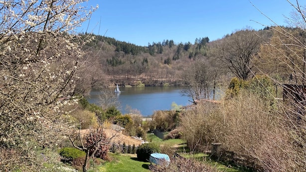 A serene lakeside view with a gazebo, trees, and a distant sailboat.