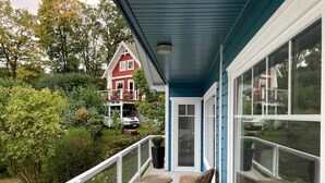 A covered balcony with wicker furniture and a view of a red house and parked cars.