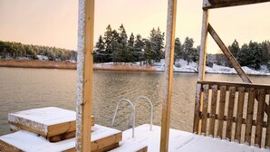 A wooden deck with steps leading to a metal ladder, overlooking a calm body of water and a forested area. - A Real Home - sea View Close to City Center (Pargas)