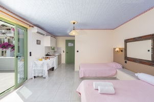 Habitación de hotel con dos camas, baño, kitchenette y balcón con flores.