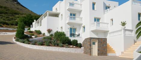A multi-story white building with balconies, a stone entrance, and a paved driveway.