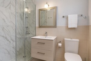 Un baño con cabina de ducha de vidrio, un lavamanos con espejo y un inodoro.