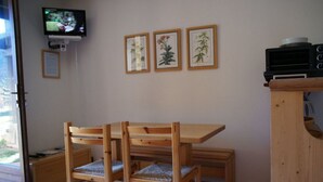 A wooden dining table with chairs, a television mounted on the wall, and framed botanical prints. - SiFa - Studio with mountain corner and terrace close to shops (Névache)
