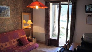A cozy living room with a sofa, a table, a lamp, and a large window with curtains. - SiFa - Studio with mountain corner and terrace close to shops (Névache)