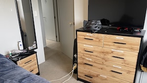 Een slaapkamer met een bed, een dressoir met gelabelde lades, een spiegel en een televisie.