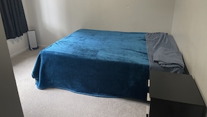 Een kleine, eenvoudig ingerichte kamer met een enkel bed, een tafeltje en een radiator.