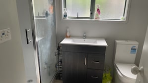 Een badkamer met een douche, wastafel, toilet en een raam met schoonmaakspullen op de vensterbank.