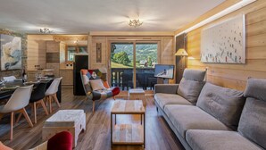 Ein gemütliches Wohnzimmer mit einer Couch, einem Esstisch und Stühlen. Ein Fernseher und ein Gemälde sind an der Wand zu sehen.