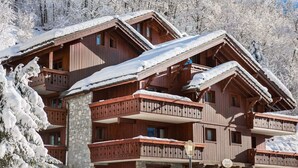 Eine mehrstöckige Holzhütte mit Balkonen, umgeben von schneebedeckten Bäumen.