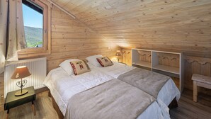 Ein Schlafzimmer einer Holzhütte mit einem Bett, Nachttischen und einem Fenster mit Vorhängen.