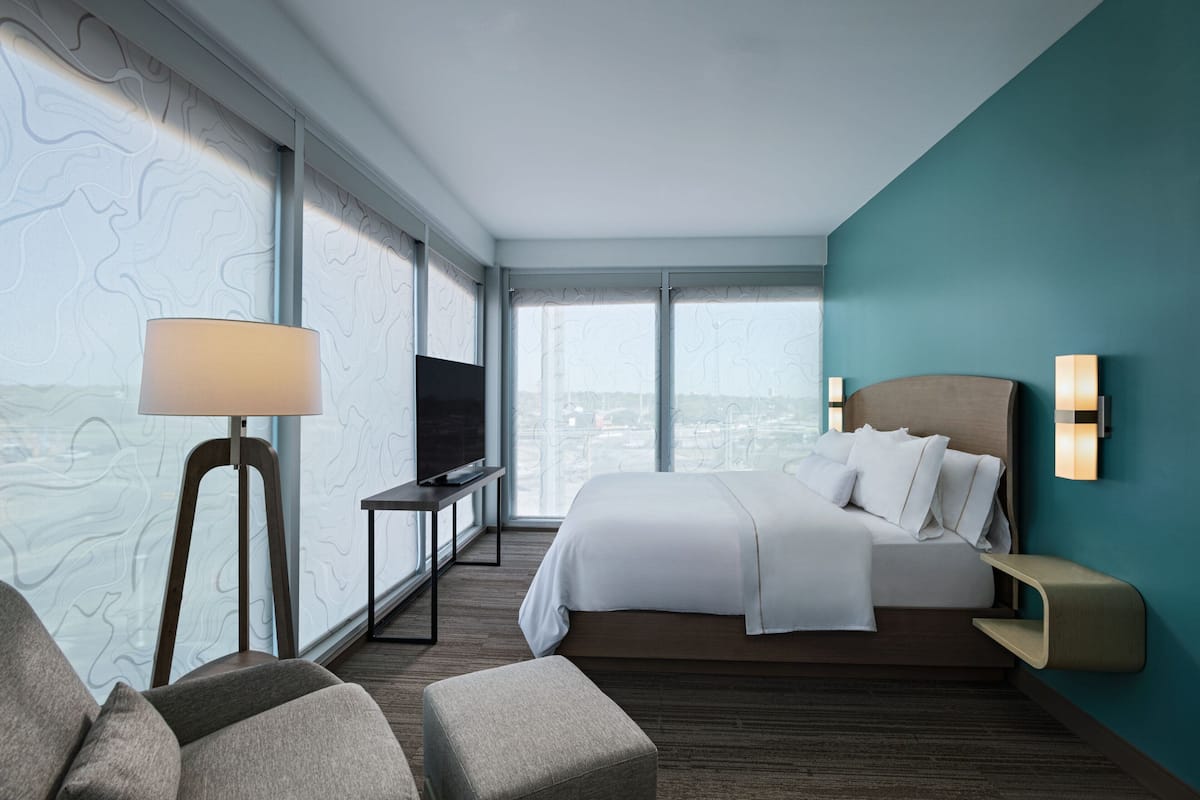 Una habitación de hotel moderna con una cama grande, televisor, escritorio y vistas a la ciudad.