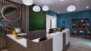 A reception area with a modern design, featuring a wooden reception desk, a green vertical garden, and a blue accent wall.