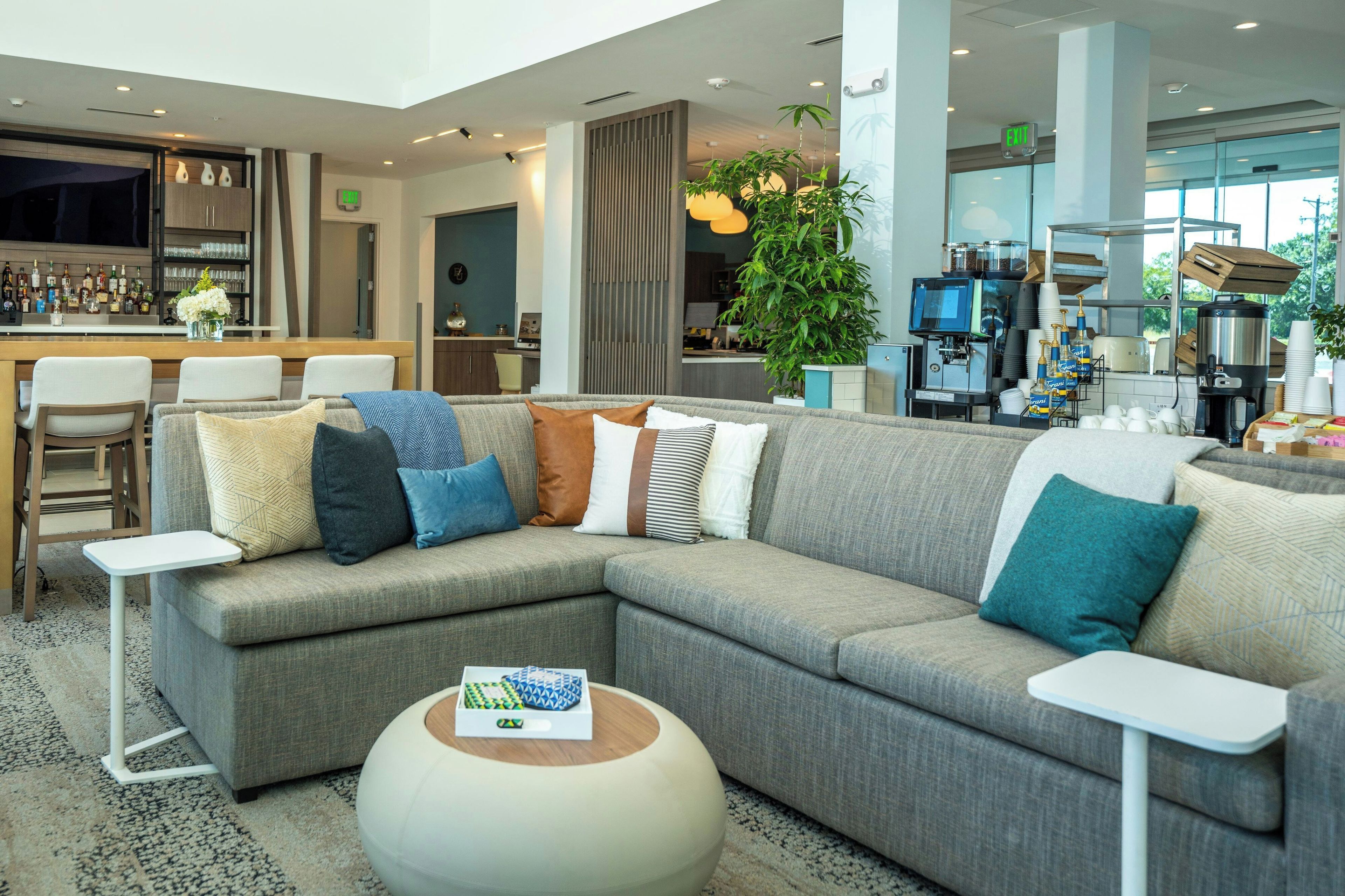 A modern hotel lobby with a sectional sofa, a bar area, and a coffee station.