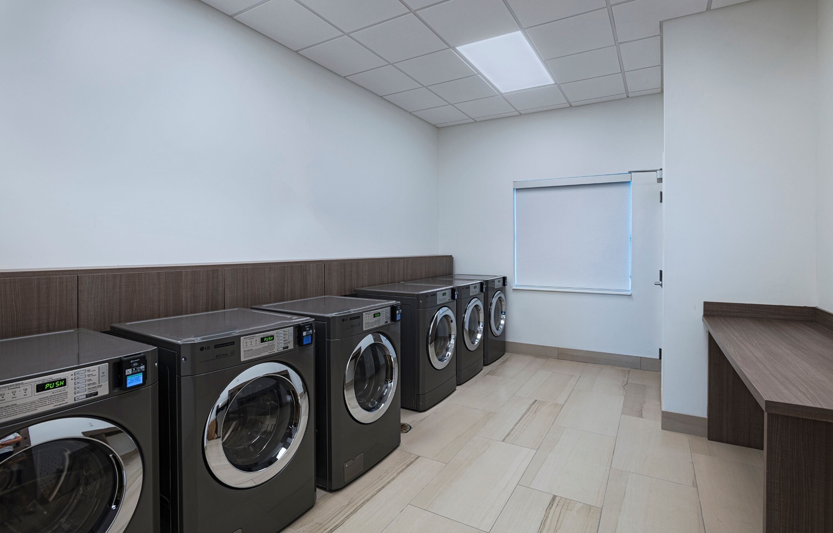 A row of front-loading washing machines in a clean, tiled laundry room with a whiteboard on the wall.