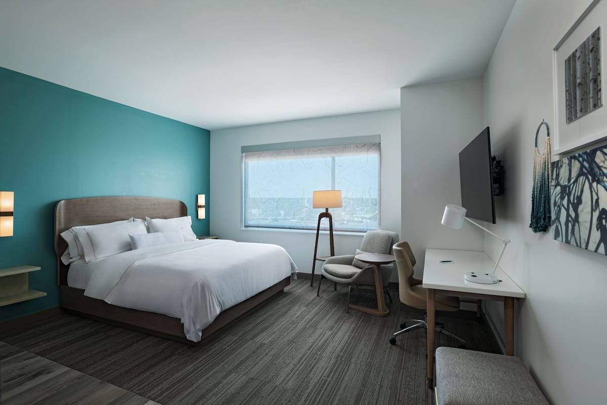 Habitación de hotel con cama, escritorio, silla, televisión y ventana con vistas.