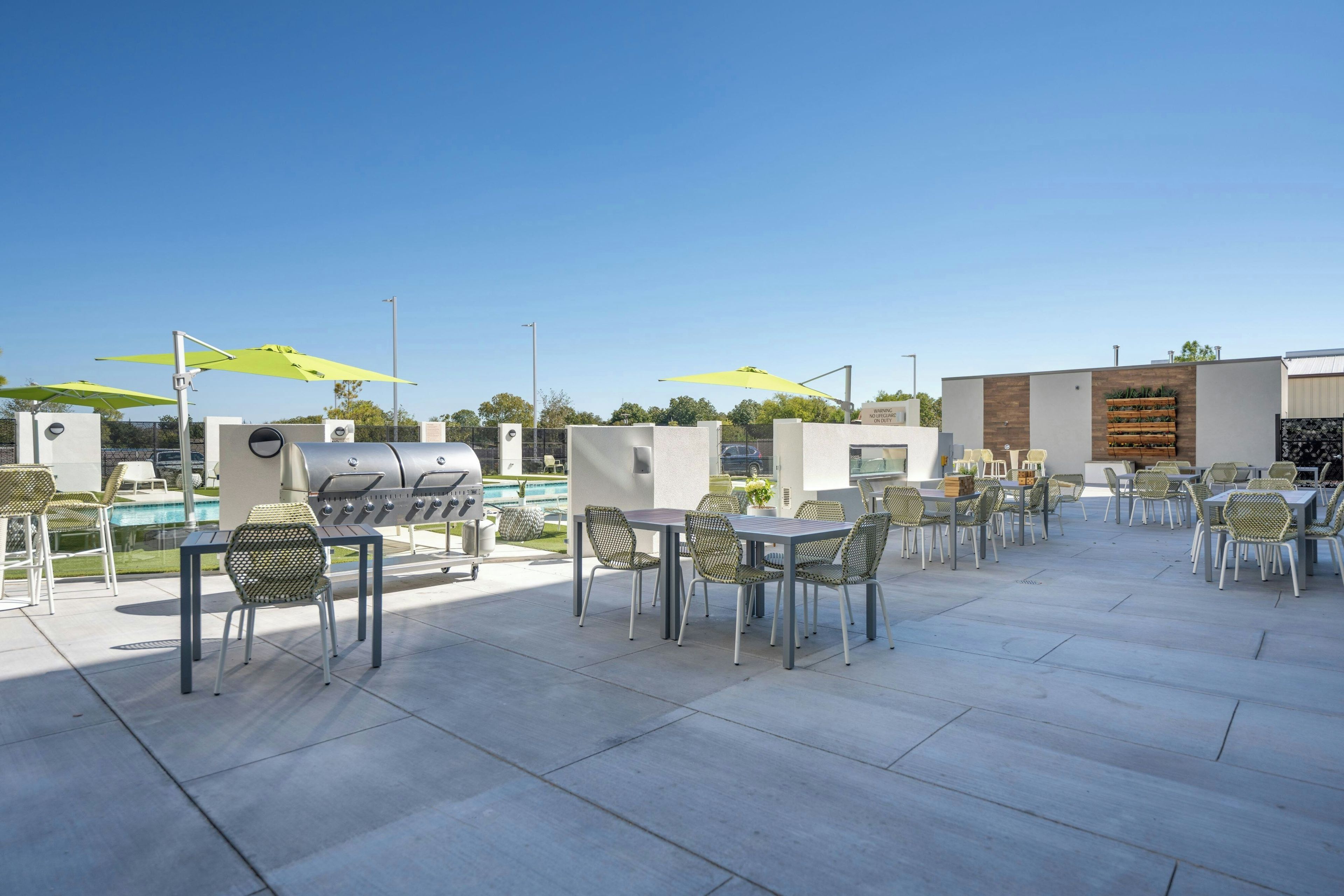 Un espacio al aire libre con mesas, sillas, una parrilla y sombrillas.