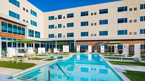 Un edificio moderno con piscina, mobiliario exterior y un cielo azul despejado.