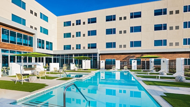 A modern building with a swimming pool, outdoor seating, and a clear blue sky.