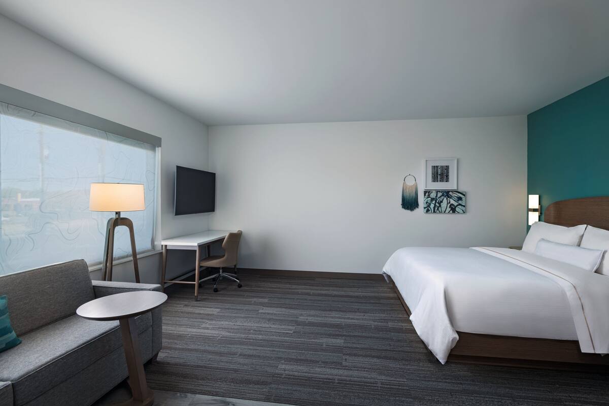Una habitación de hotel con cama, escritorio, silla, sofá, televisor y obras de arte en la pared.