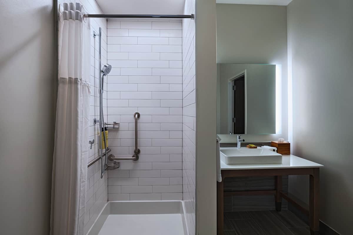 Un baño moderno con paredes de azulejos blancos, ducha con puerta de cristal, lavabo blanco y tocador de madera.