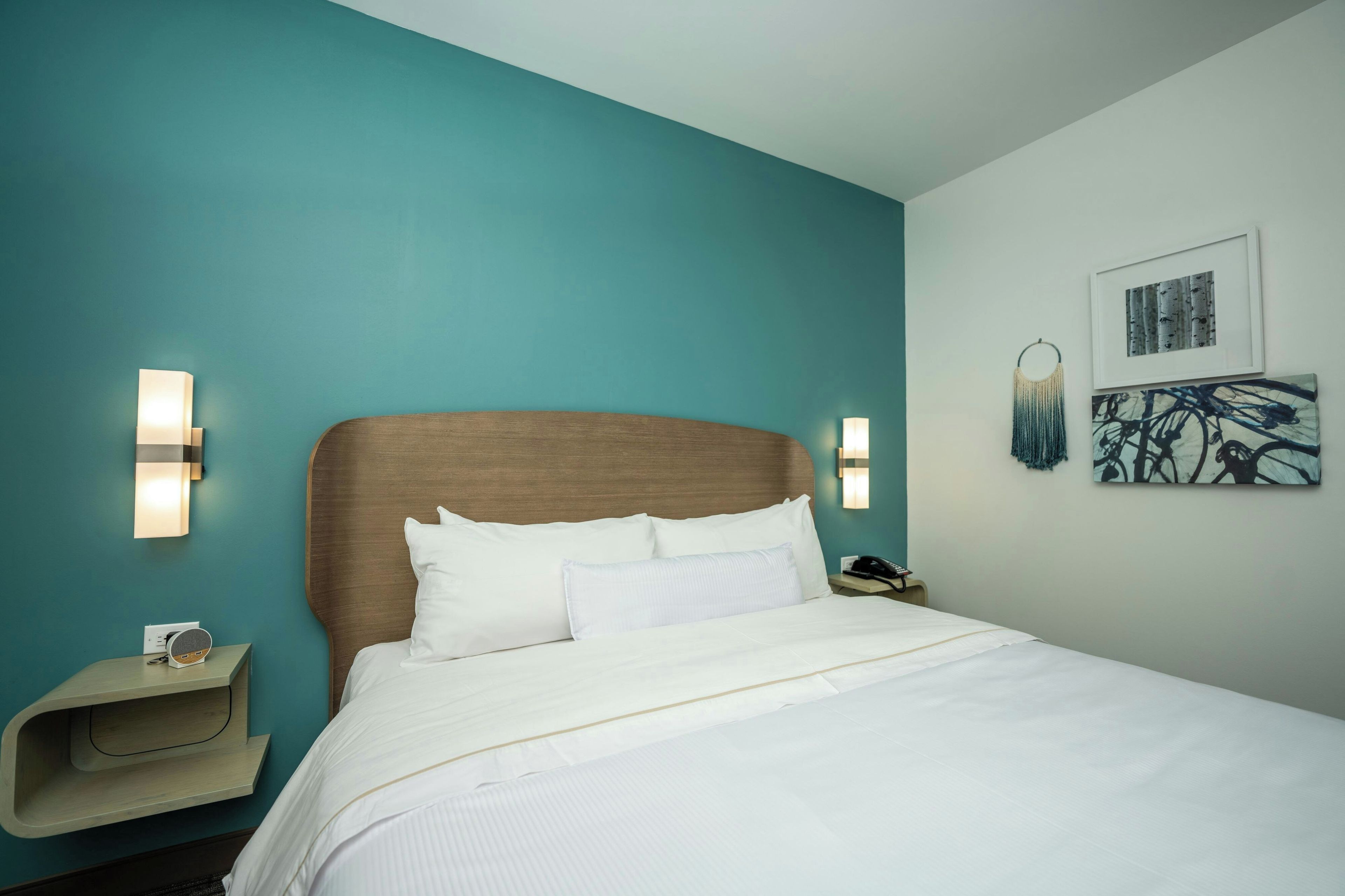 Een hotelkamer met een bed, nachtkastje, telefoon en wandlampen.