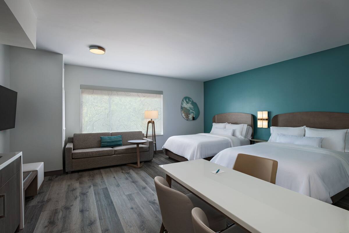 Habitación de hotel con dos camas, un sofá, un escritorio y un televisor.