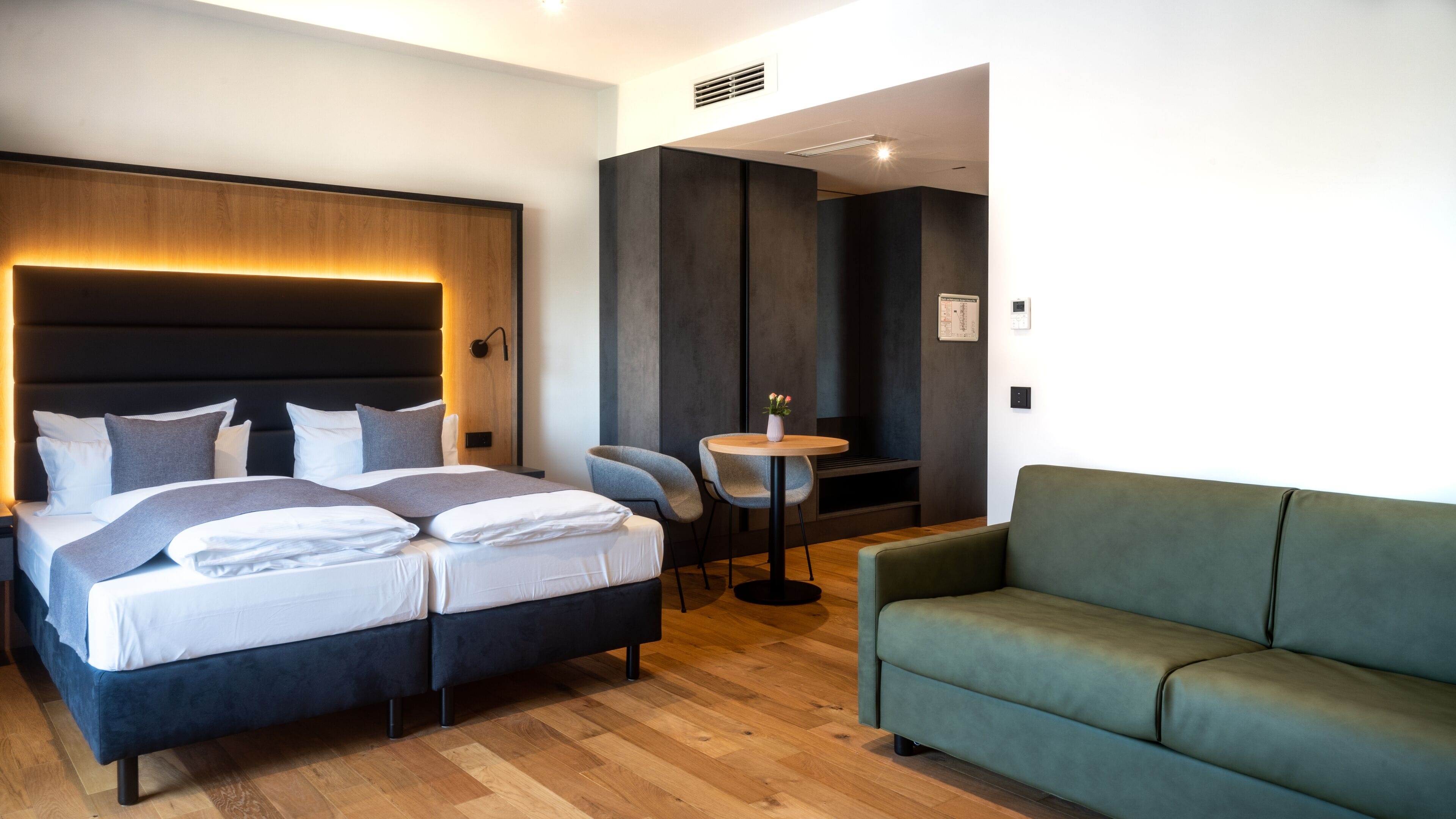Una camera d'albergo moderna con un letto grande, un divano verde e un tavolino rotondo con un vaso.