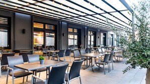 An outdoor cafe with tables and chairs, a pergola with lights, and a view of the street. - Burgau Hotel Sonnenhof (Burgau)