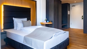 A modern bedroom with a large bed, bedside tables, a small round table, and a built-in bench. - Burgau Hotel Sonnenhof (Burgau)