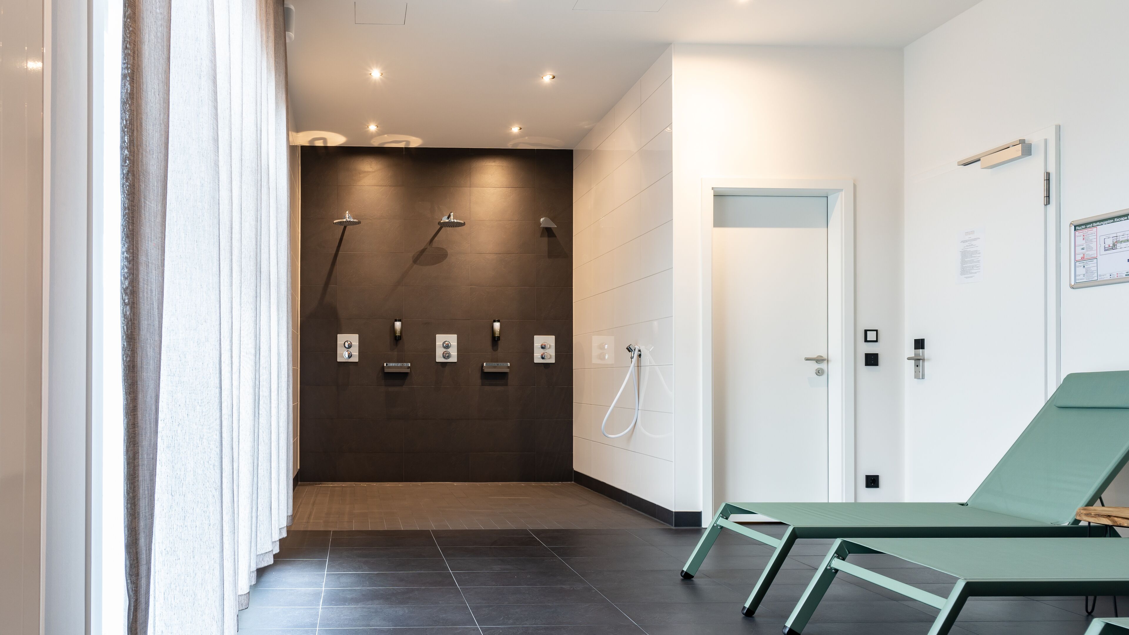 Ein modernes Badezimmer mit Duschbereich, einem grünen Lounge-Sessel und einer weißen Tür.