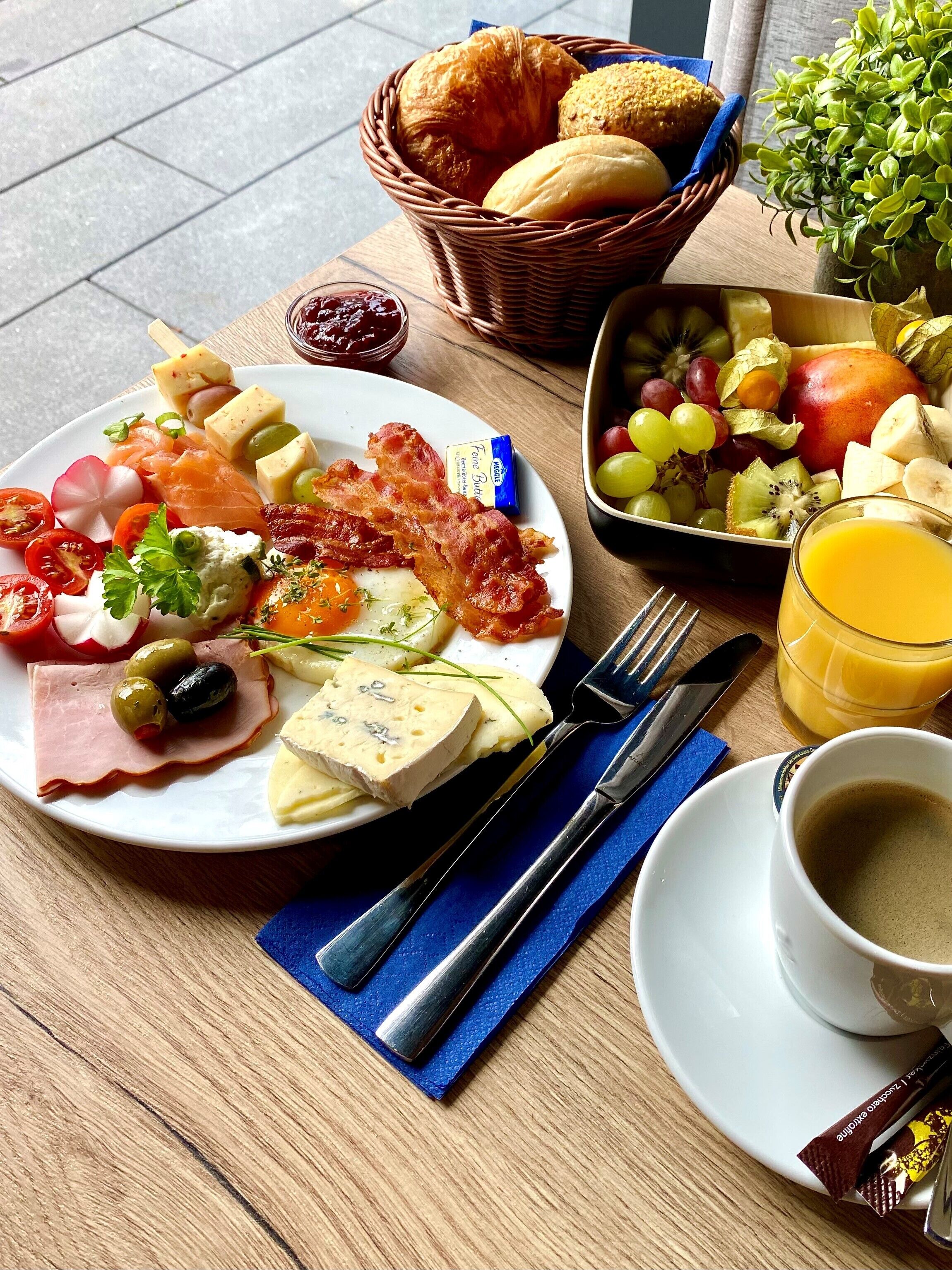 A breakfast table with a plate of food, a basket of bread, a bowl of fruit, a glass of orange juice, and a cup of coffee.