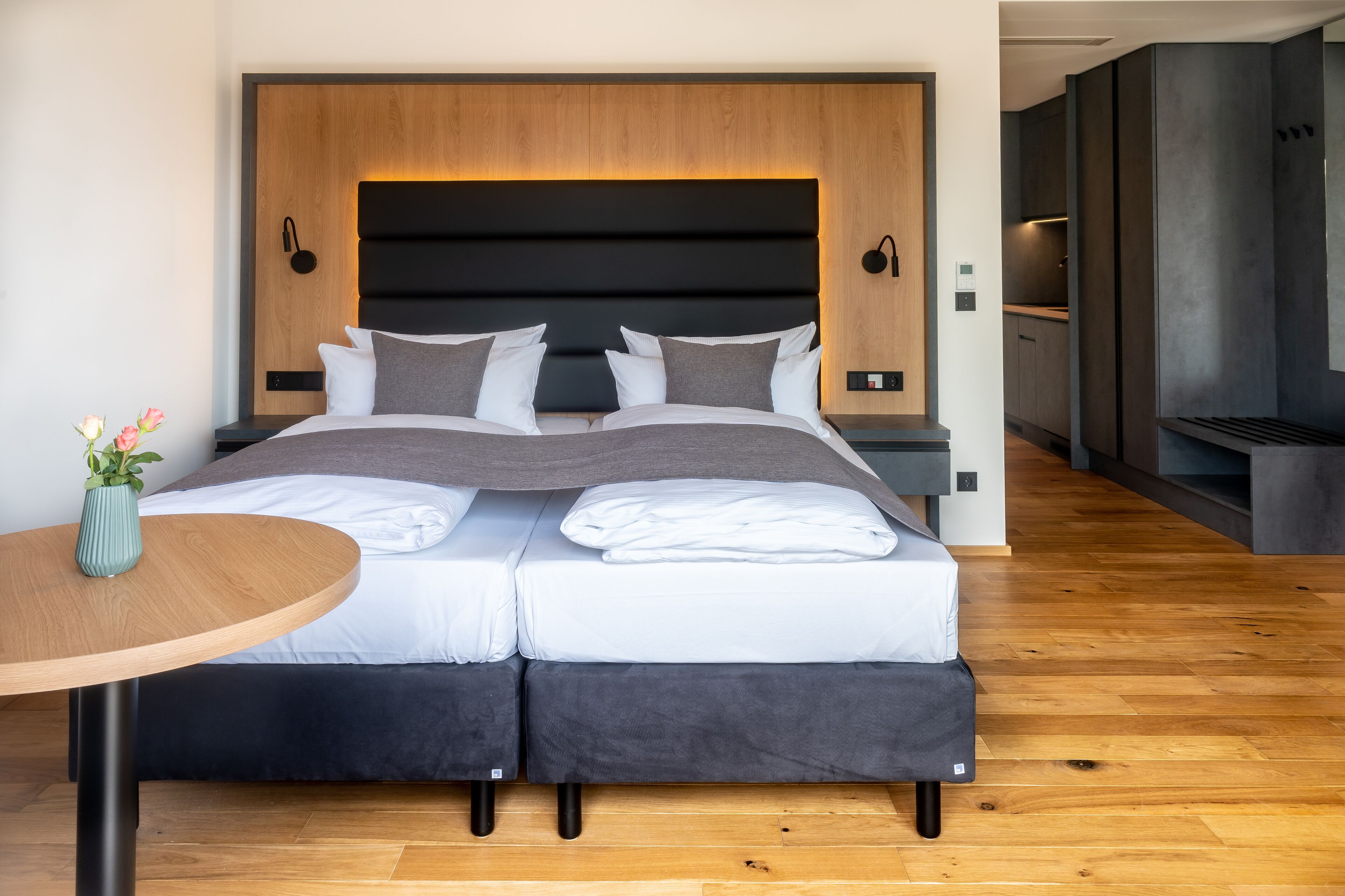 A modern hotel room with a large bed, a small table, and a vase of flowers.