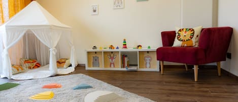 A room with a white canopy tent, a red sofa, and a play area with toys and a bookshelf.