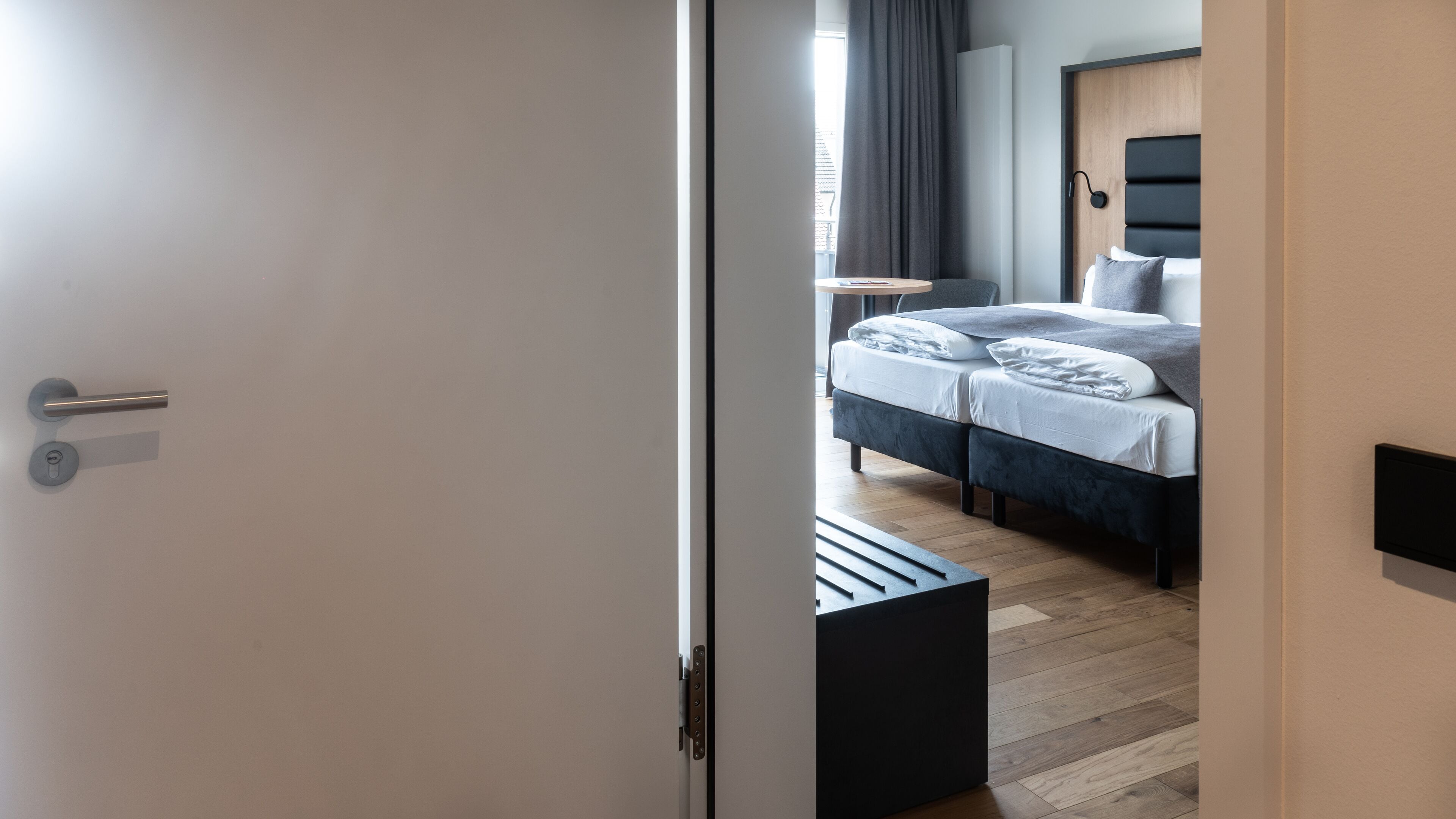 A modern bedroom with a bed, bedside table, and a view of the outside.