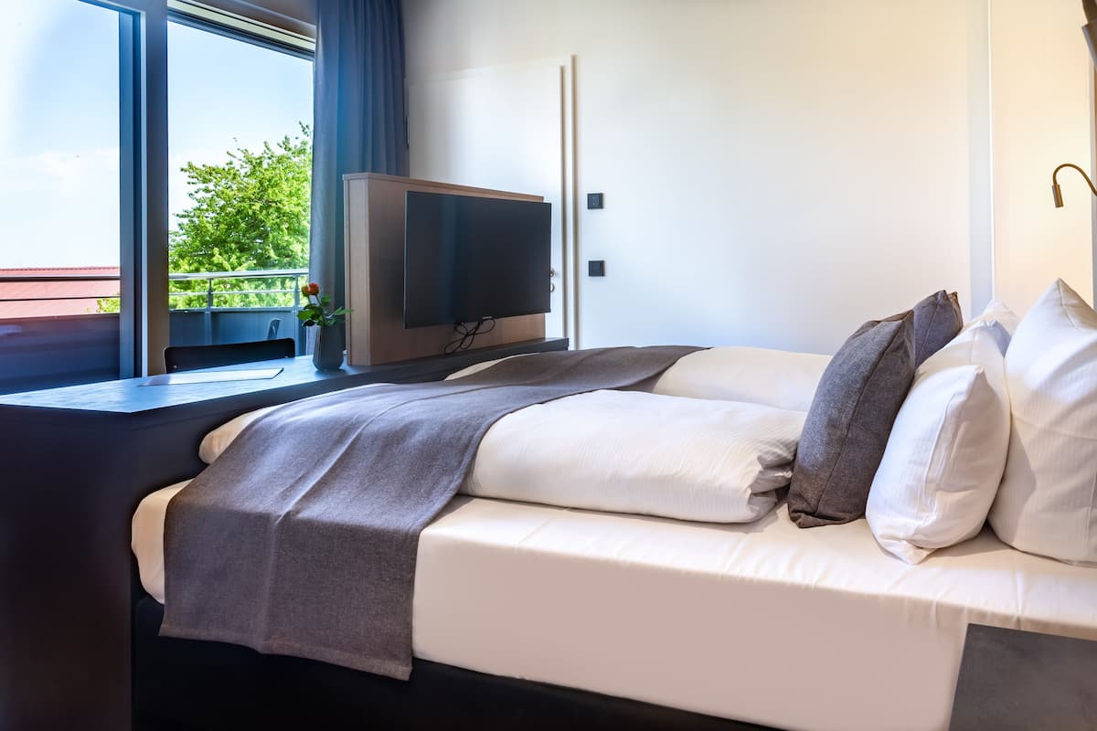 Une chambre d’hôtel moderne dotée d’un grand lit, d’une télévision à écran plat et d’un balcon offrant une vue sur la verdure.