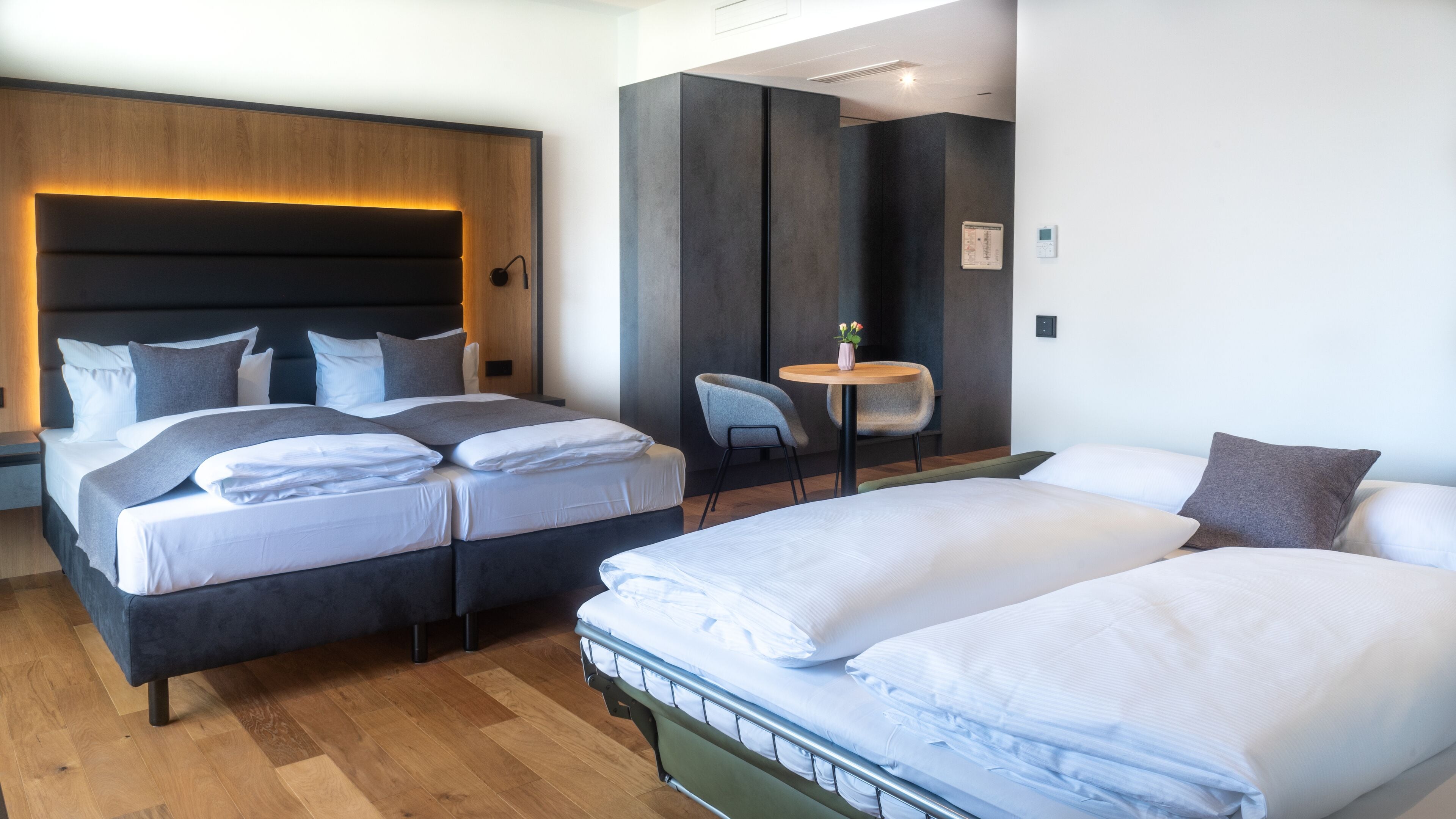 A modern hotel room with two beds, a small table, and a chair.